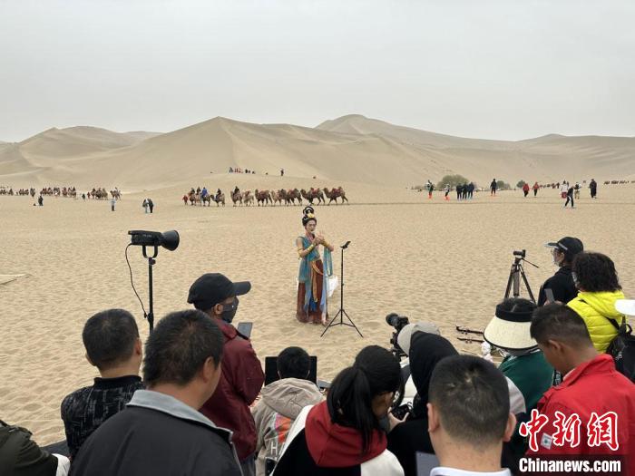圖為2023年4月底,敦煌大漠“逐舞者”奧楠在鳴沙山月牙泉景區視頻直播,吸引游人圍觀。 馮志軍 攝 圖為2023年4月底,敦煌大漠“逐舞者”奧楠在鳴沙山月牙泉景區視頻直播,吸引游人圍觀。 馮志軍 攝